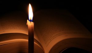 an open Bible in partial darkness with a lighted candle